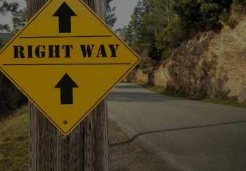Yellow road sign reading RIGHT WAY with arrows pointing forward on winding mountain road symbolizing correct path