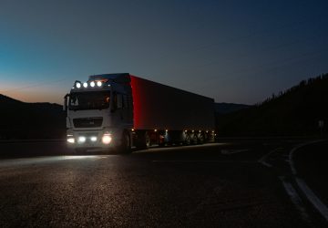 Semi truck with red trailer and bright lights on highway at dusk representing fast EDI processing for trucking logistics