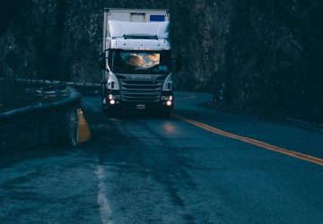 Scania truck with headlights on dark mountain road representing accelerated EDI response times in trucking logistics